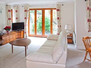 A living room with a white sofa wooden coffee table television and wooden dining chairs at 9 Bancroft Place in Stratford upon Avon