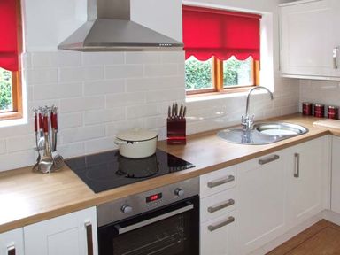 A kitchen with a wooden countertop a stovetop with a pot a stainless steel oven a knife block a sink and red window blinds at 9 Bancroft Place in Stratford upon Avon