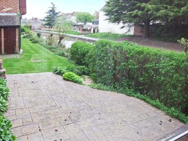 A patio with paving stones next to a lawn and hedges by a canal at 9 Bancroft Place in Stratford-upon-Avon