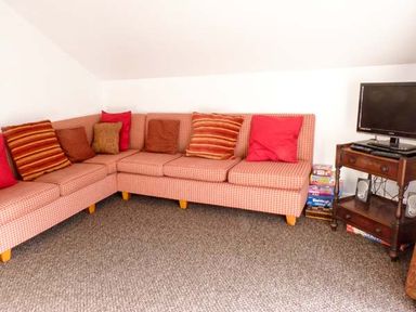 A corner seating area with a checkered sofa with multiple cushions and a wooden TV stand with a television and board games at Woodstone Barn Whitchurch near Tavistock