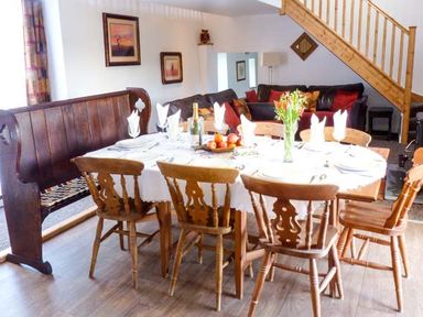 A dining area with a wooden table set with plates and napkins surrounded by wooden chairs and a wooden bench at Woodstone Barn in Whitchurch near Tavistock