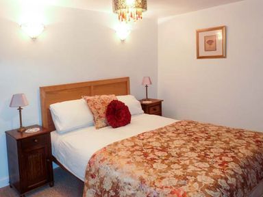 A bedroom with a double bed and floral bedding two bedside tables with lamps and a framed picture on the wall at Woodstone Barn Whitchurch near Tavistock