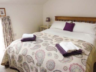 A bedroom with a bed covered in a patterned bedspread and folded towels at Woodstone Barn in Whitchurch near Tavistock
