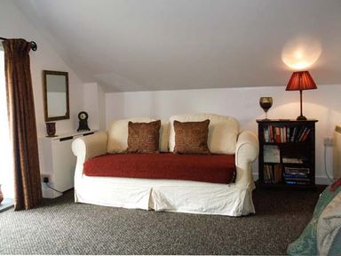 A living room with a sofa a side table with books and a lamp and a mirror on the wall at Woodstone Barn in Whitchurch near Tavistock