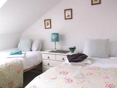 A bedroom with two single beds a nightstand with a lamp and decorative items and framed pictures on the wall at Woodstone Barn Whitchurch near Tavistock