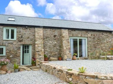 Stone barn exterior with green door windows potted plants bench and gravel courtyard at Woodstone Barn Whitchurch near Tavistock