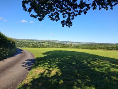 A view of a road and grassy field with hills in the background at Woodstone Barn Whitchurch near Tavistock