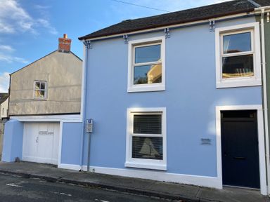 A blue house with white window frames and a dark door next to a garage with white doors on a street
