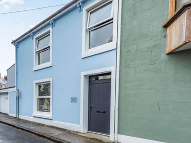The exterior of a blue two-story building with white trim and a gray door next to a green wall on a street at Barafundle House Tenby