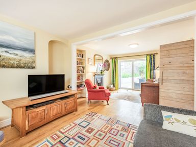 A living room with a wooden TV stand a red armchair and sliding glass doors leading outside at Barafundle House in Tenby