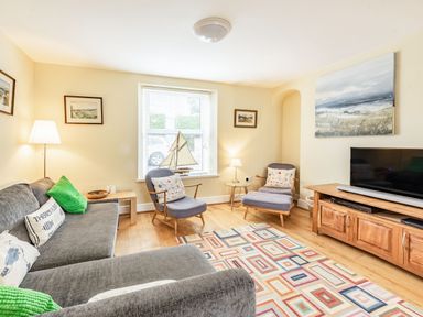 A living room with gray sofa green cushions armchairs a wooden TV stand and a colorful rectangular rug at Barafundle House in Tenby