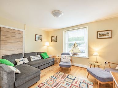 A living room with a grey sofa green cushions armchairs a model sailboat on the window sill and a patterned rug at Barafundle House in Tenby