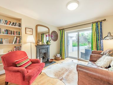 A living room with a red armchair, leather sofa, fireplace, bookshelf, floor lamp, and sliding glass doors at Barafundle House in Tenby
