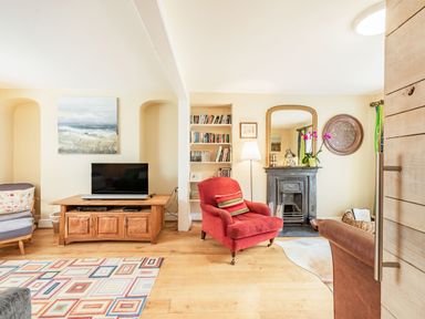 A living room with a television on a wooden cabinet a red armchair a fireplace and bookshelf at Barafundle House in Tenby