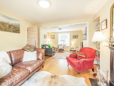 A living room with brown leather sofa red armchair wooden flooring and a small area rug at Barafundle House in Tenby