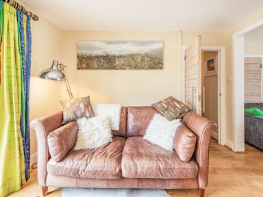 A living room with a brown leather sofa with cushions and a lamp next to colorful curtains at Barafundle House in Tenby