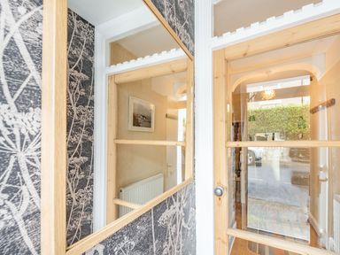 A hallway with a wooden framed glass door and a large mirror on a wallpapered wall at Barafundle House in Tenby
