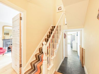 A hallway with striped carpeted stairs next to a wooden door open to a living room and a tiled floor leading to a kitchen at Barafundle House in Tenby