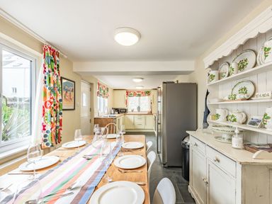 A kitchen with a wooden dining table set with plates and glasses next to a cabinet with decorative plates at Barafundle House in Tenby