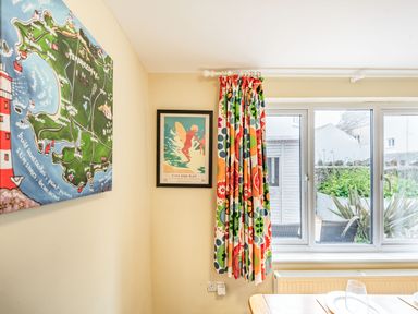A dining area with a window and colorful floral curtain two framed artworks on the wall and a glimpse of outdoor greenery