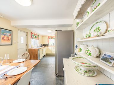 A kitchen with wooden dining table set with plates and glasses and shelves with china at Barafundle House in Tenby