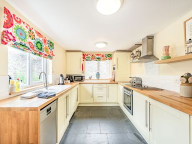 A kitchen with wooden countertops white cabinets and floral patterned window blinds at Barafundle House in Tenby