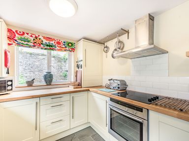 A kitchen with white cabinets wooden countertops a window with colorful floral blinds and stainless steel appliances at Barafundle House in Tenby