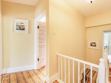 A hallway with wooden floor and white stair railing with two framed pictures on the walls at Barafundle House in Tenby