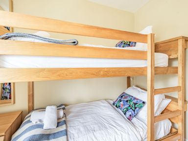 A bedroom with bunk beds wooden frame white bedding and striped blanket at Barafundle House in Tenby