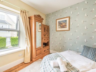 A bedroom with a window beige curtains a wooden wardrobe with a mirror bed with patterned bedding and a wall with seagull wallpaper at Barafundle House in Tenby
