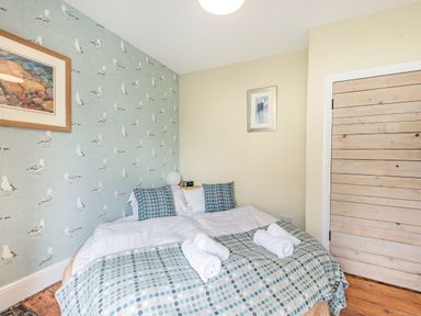 A bedroom with a double bed two rolled towels seaside themed wallpaper and a wooden door at Barafundle House in Tenby