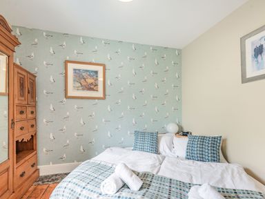 A bedroom with a double bed with white bedding and blue pillows near a wooden wardrobe and seagull wallpaper at Barafundle House in Tenby