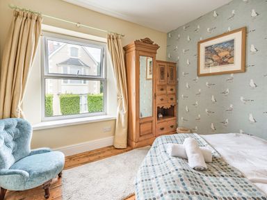 A bedroom with a blue armchair wooden wardrobe bed with rolled towels and seagull wallpaper at Barafundle House in Tenby