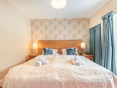 A bedroom with a double bed two bedside tables with lamps and blue curtains at Barafundle House in Tenby