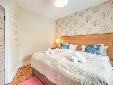 A bedroom with a double bed with pillows and towels a wooden headboard floral wallpaper and a wooden floor at Barafundle House in Tenby
