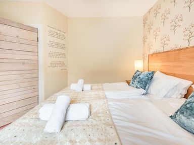 A bedroom with a wooden bed headboard white bedding blue pillows rolled white towels a bedside lamp and floral wallpaper at Barafundle House in Tenby