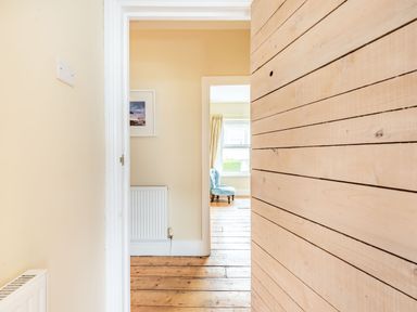 A hallway with wooden floor and walls leading to a room with a blue chair near a window at Barafundle House in Tenby