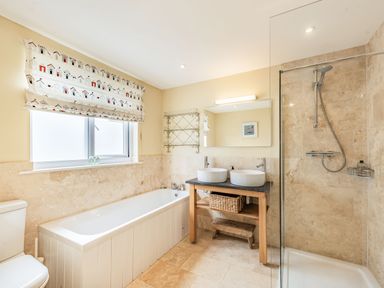A bathroom with a bathtub a shower area two sinks with a wooden stand and a toilet at Barafundle House in Tenby