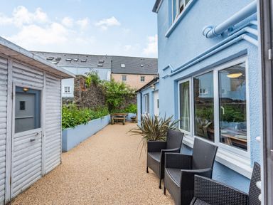 An outdoor patio area with black wicker chairs a wooden shed planter with plants and a picnic table at Barafundle House in Tenby