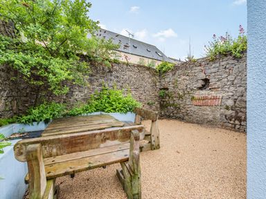 An outdoor patio area with a wooden bench and table surrounded by stone walls and plants at Barafundle House in Tenby