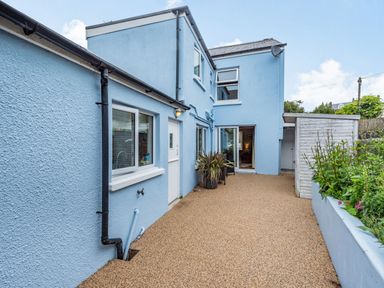 An outdoor patio area with a blue two-story house a shed and plants on the side at Barafundle House in Tenby