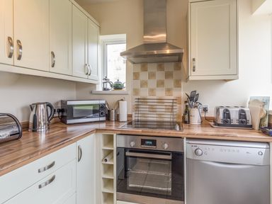 A kitchen with wooden countertops white cabinets a microwave kettle toaster oven and dishwasher at Dune View in Beadnell