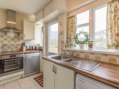 A kitchen with a stainless steel oven dishwasher sink and window with floral curtains at Dune View in Beadnell