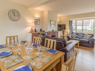 A dining table set with glassware and blue napkins next to a living area with leather sofas and a television at Dune View in Beadnell