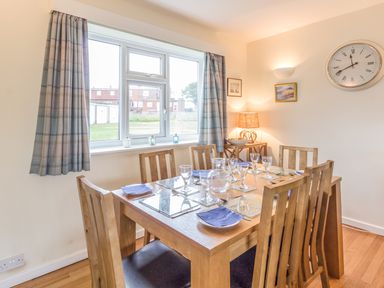A dining room with wooden table and six chairs set with plates and glasses at Dune View in Beadnell