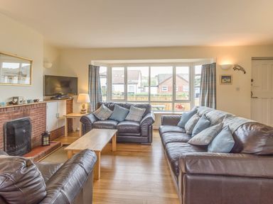 A living room with brown leather sofas a wooden coffee table a brick fireplace and a television at Dune View in Beadnell