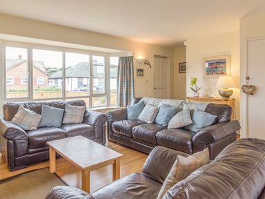 A living room with three leather sofas a wooden coffee table and a sideboard with a lamp at Dune View in Beadnell