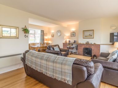 A living room with brown leather sofas a plaid throw a brick fireplace and a dining table at Dune View in Beadnell