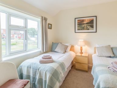 A bedroom with two single beds a nightstand with a lamp and a window at Dune View in Beadnell