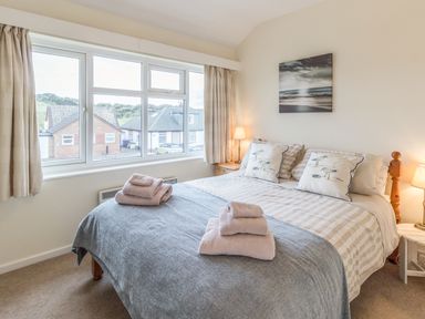 A bedroom with a double bed two bedside tables lamps and a window showing houses outside at Dune View in Beadnell
